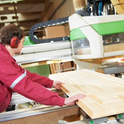 industrial carpenter worker operating wood cutting machine during wooden door furniture manufacturing